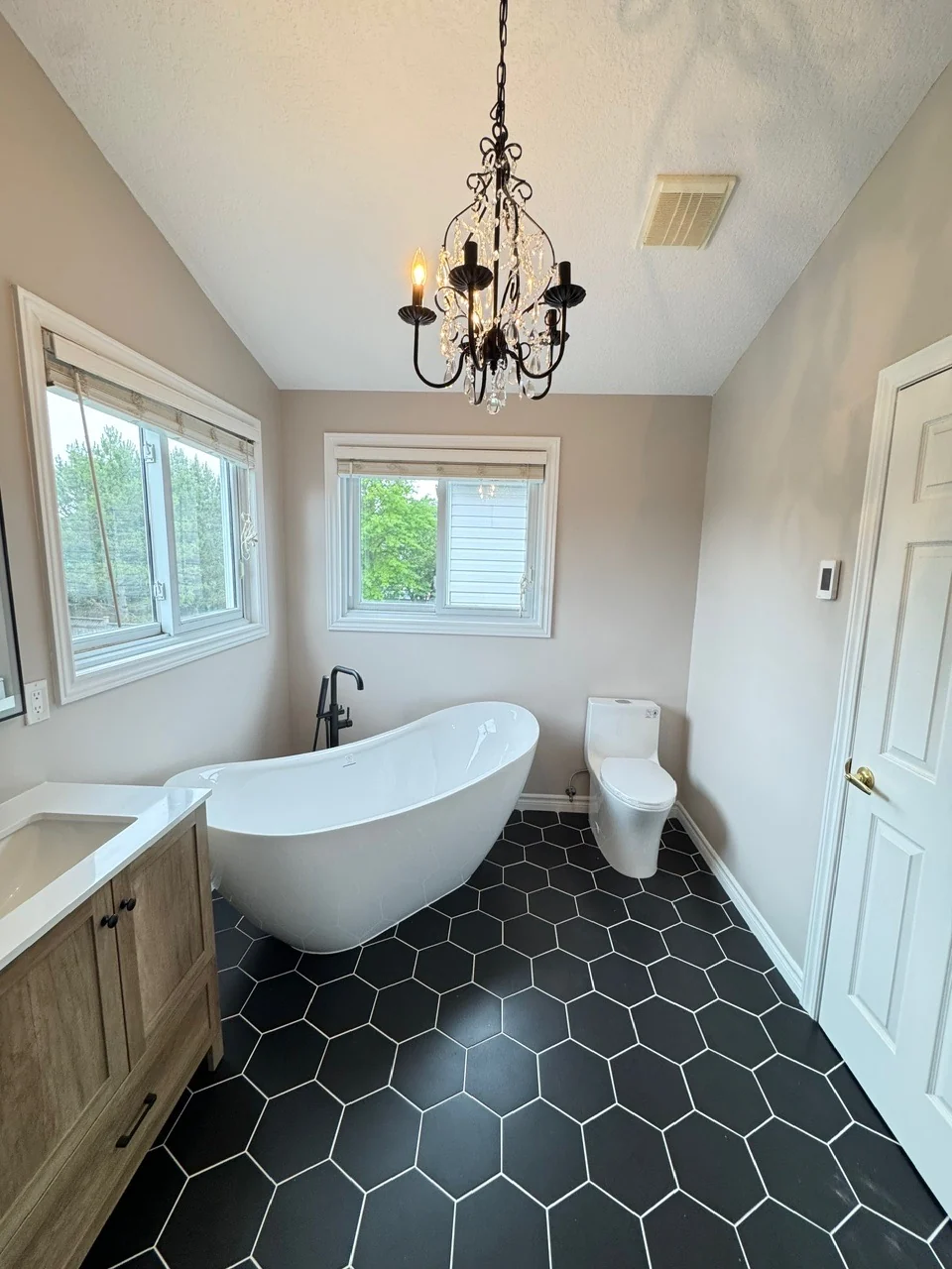 Renovated bathroom with a freestanding white tub, black floor-mounted faucet and hexagonal floor tiles