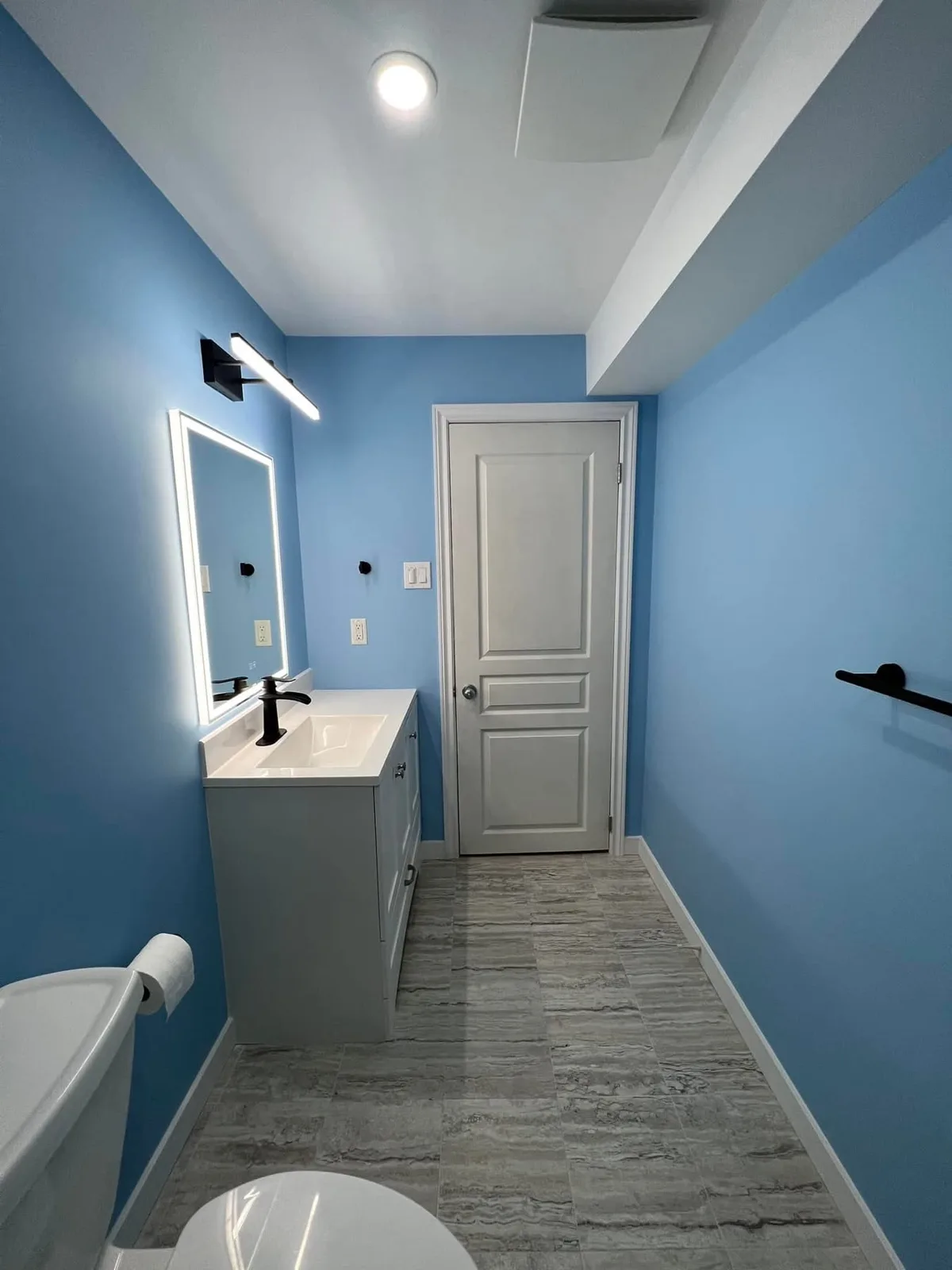 Grey bathroom vanity with an illuminated mirror and black faucet